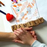 Child holding hand of adult person, family word made from cubes on house picture